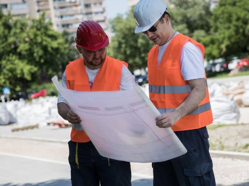 Land surveyor reviewing property plans with a builder at a residential construction site